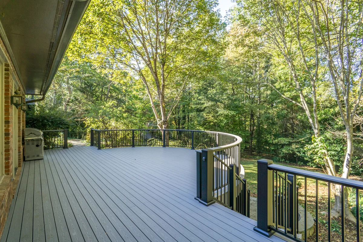 Curved Westbury Tuscany railing and decorative posts on a deck surrounded by woodland